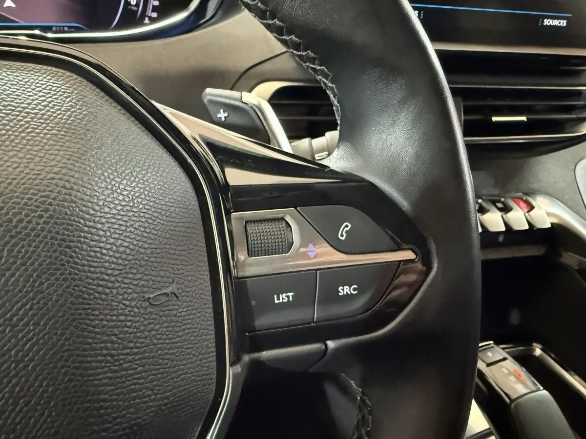 Gros plan sur le volant cuir noir côté gauche du Peugeot 5008 2021 avec commandes audio et palettes au volant.