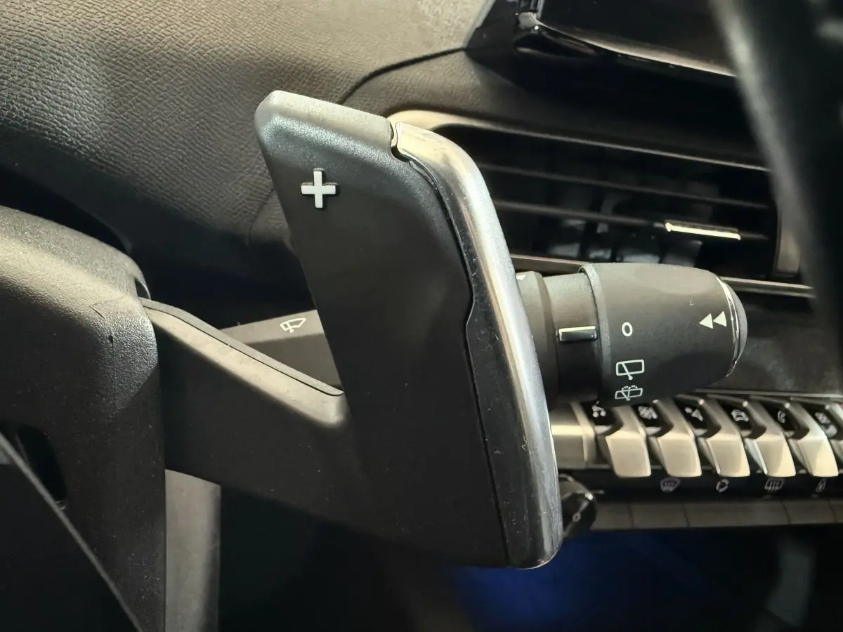 Gros plan sur la palette de changement de vitesse + côté droit du volant noir dans l’habitacle d’un Peugeot 5008 gris clair.