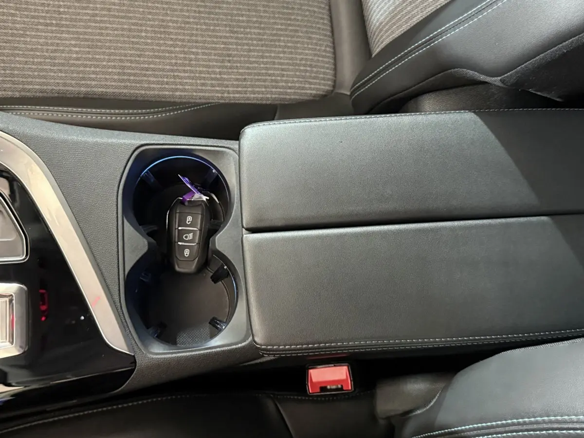 Vue rapprochée de la console centrale noire avec porte-gobelets et clé de voiture Peugeot 5008 posée dedans.