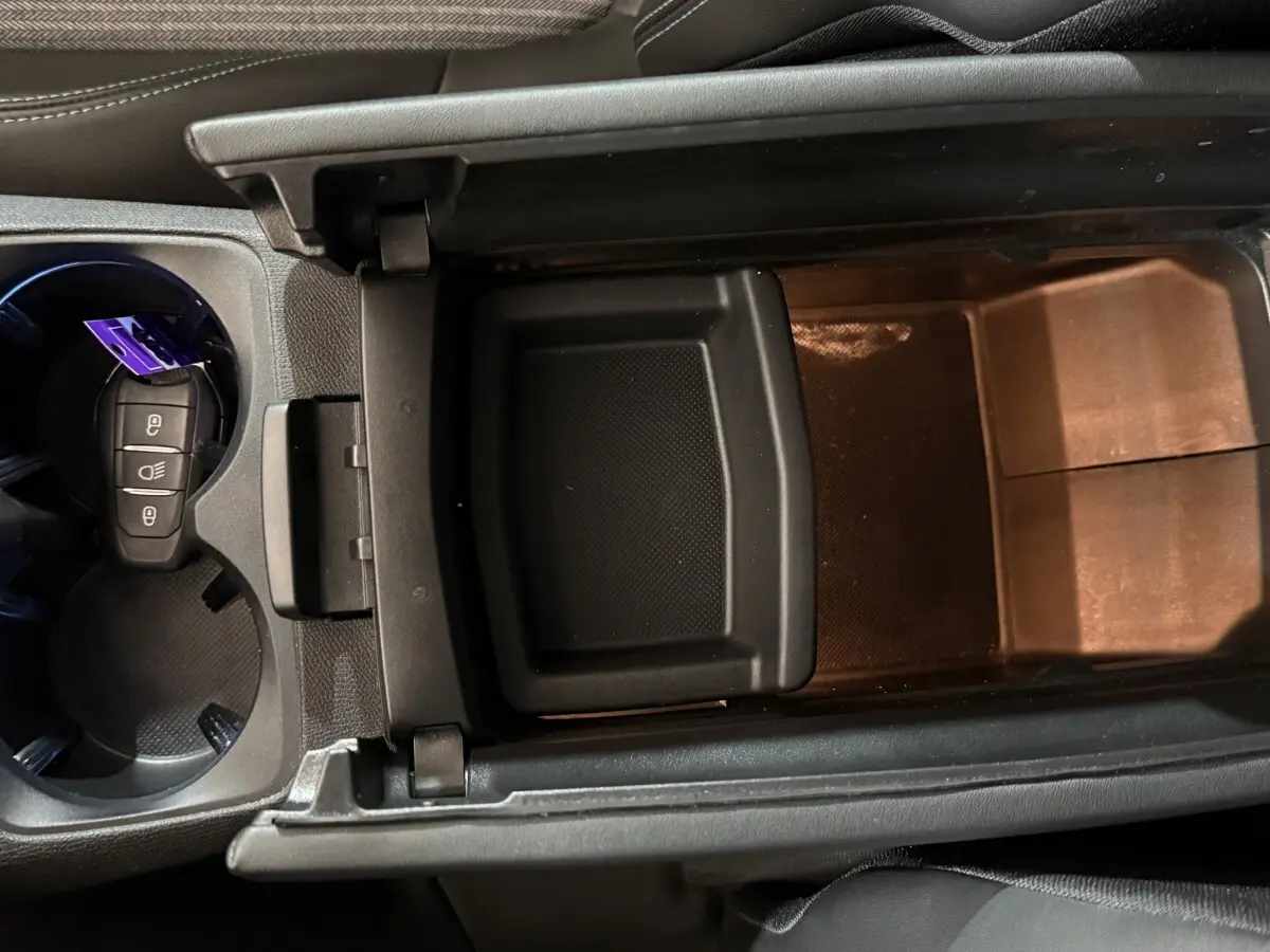 Vue rapprochée de la console centrale ouverte du Peugeot 5008 gris clair, avec porte-clés dans porte-gobelets.