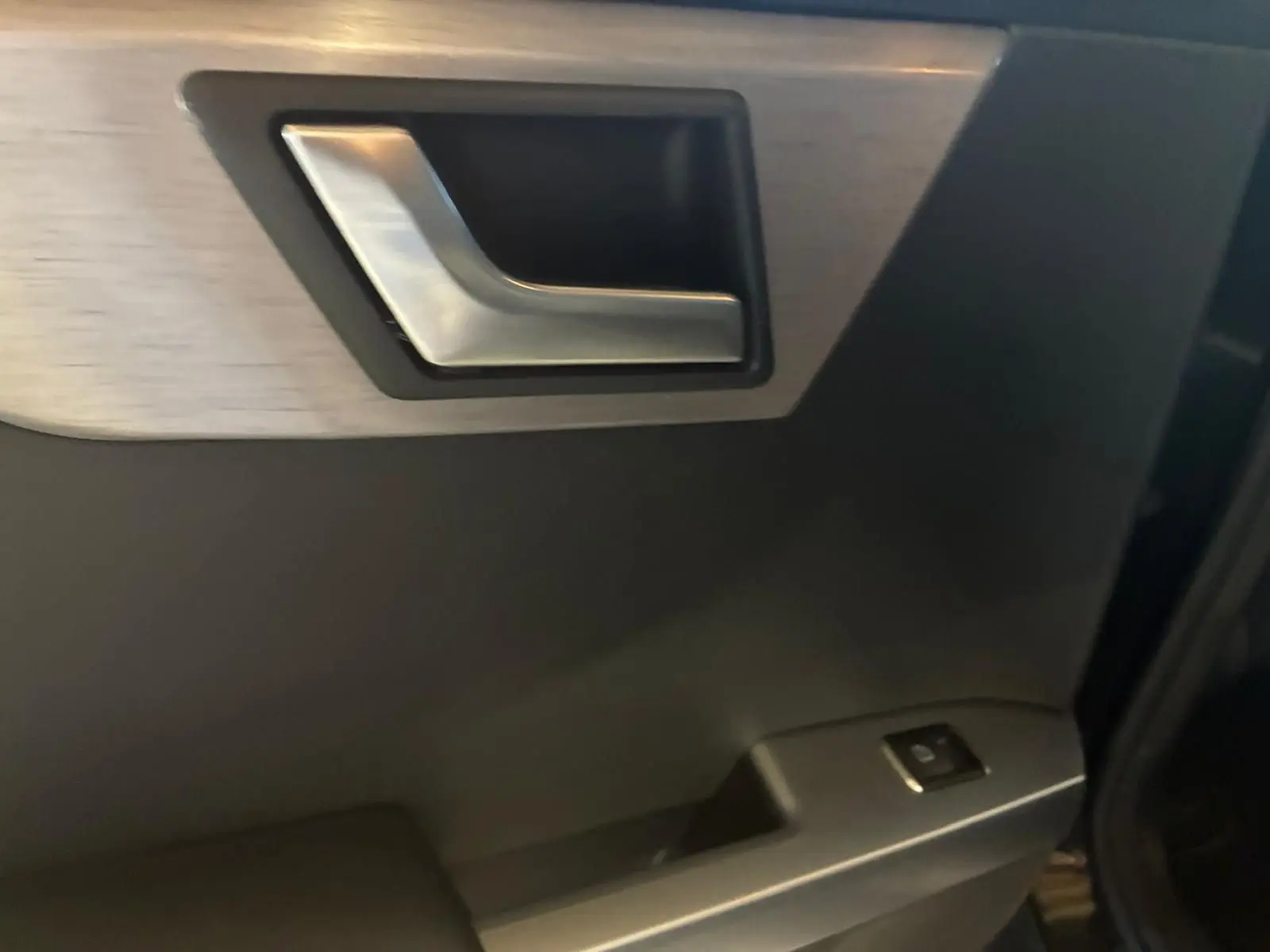 Gros plan sur la poignée intérieure en métal brossé et le panneau de porte noir du Mercedes GLK 220 CDI 2012.