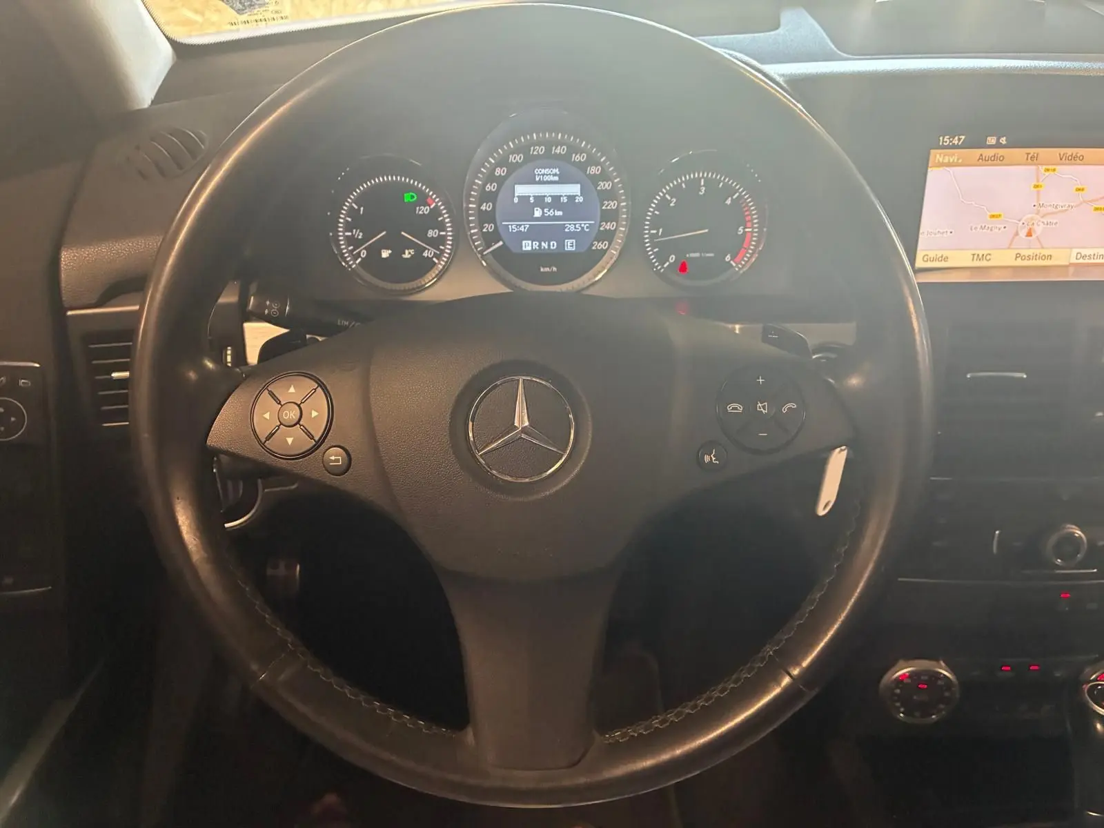 Vue rapprochée du volant noir de Mercedes GLK 220 CDI 2012 avec tableau de bord et écran GPS allumé.