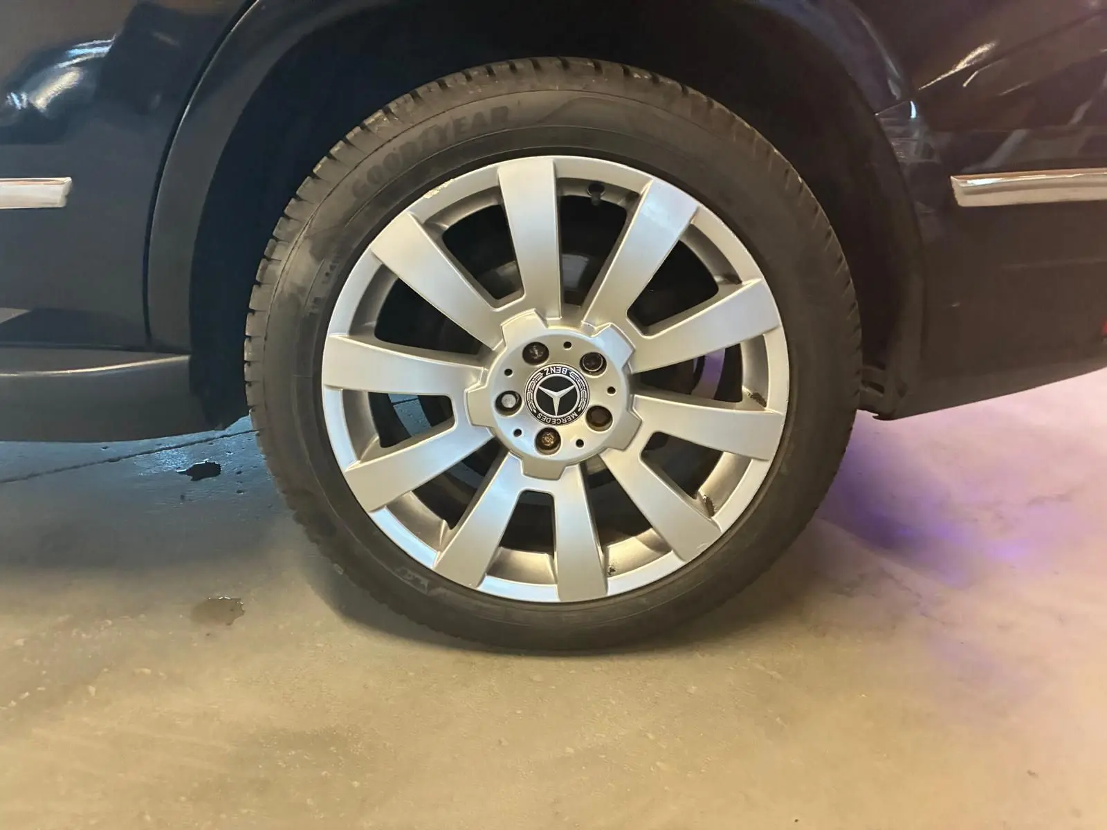Gros plan sur la roue avant droite argentée d’un Mercedes GLK noir, mettant en valeur la jante étoile et le logo central.
