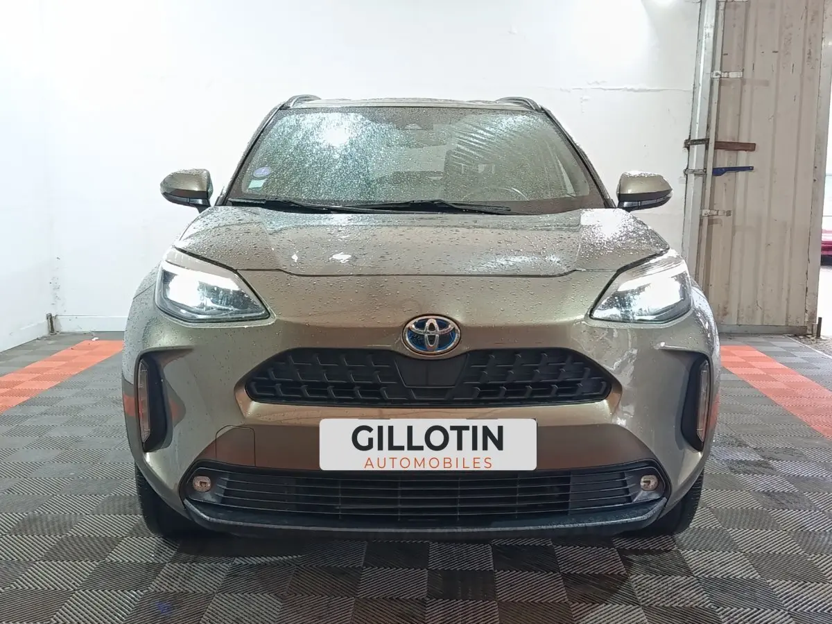 Vue frontale d'une Toyota Yaris Cross gris foncé avec phares LED allumés dans un garage.