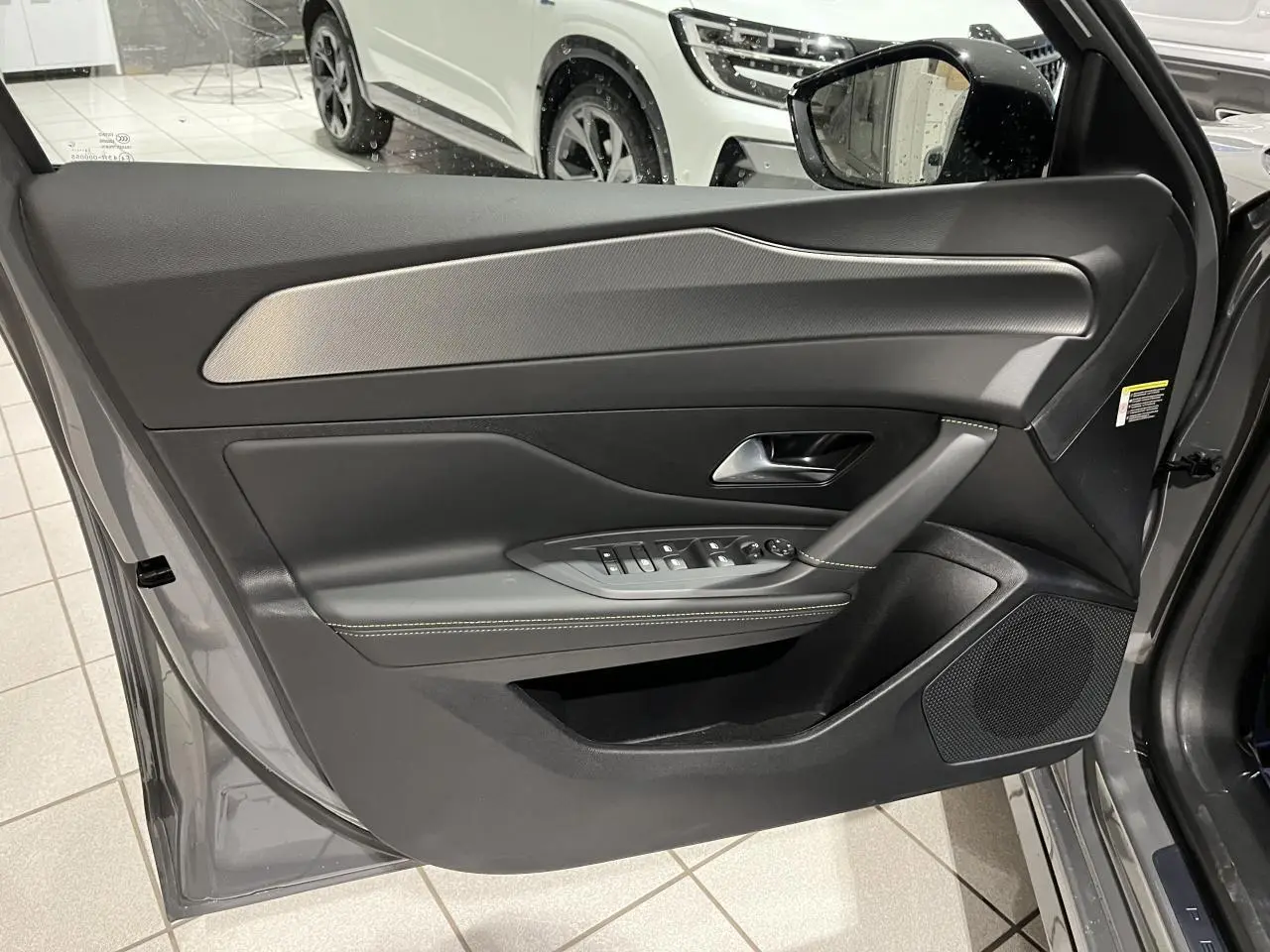 Porte avant gauche ouverte d'une Peugeot 308 gris selenium, avec garniture noire et surpiqûres claires.