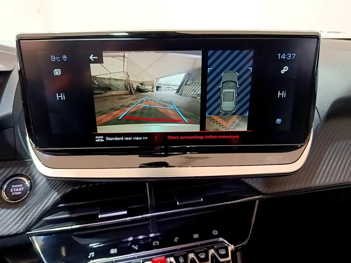 Vue intérieure du tableau de bord du Peugeot 2008 blanc, écran tactile affichant la caméra de recul et l’aide au stationnement.