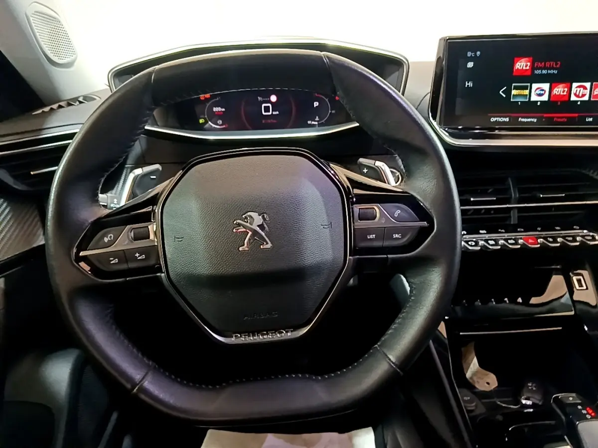 Vue rapprochée du volant cuir multifonctions noir et du tableau de bord numérique du Peugeot 2008 blanc 2021.