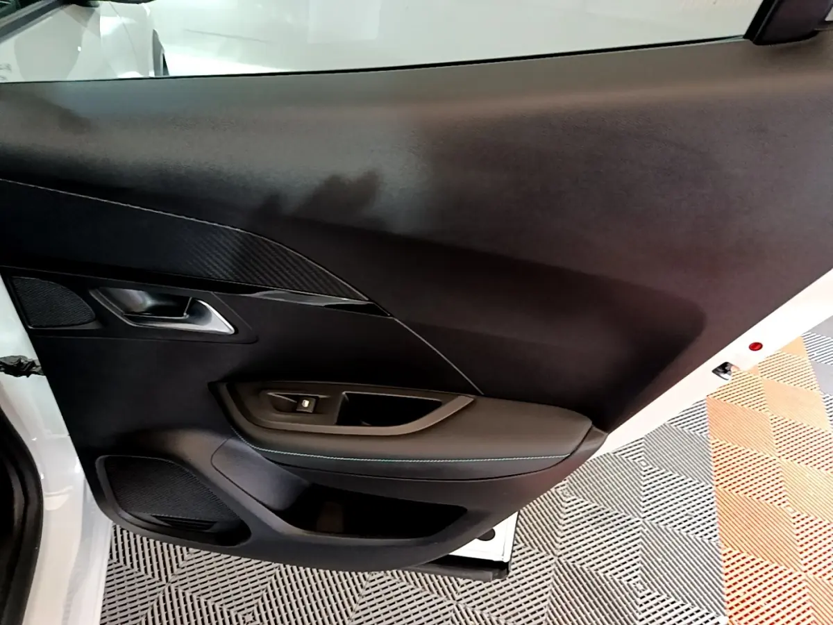 Vue intérieure de la porte avant gauche du Peugeot 2008 blanc, avec garniture noire et poignée argentée.