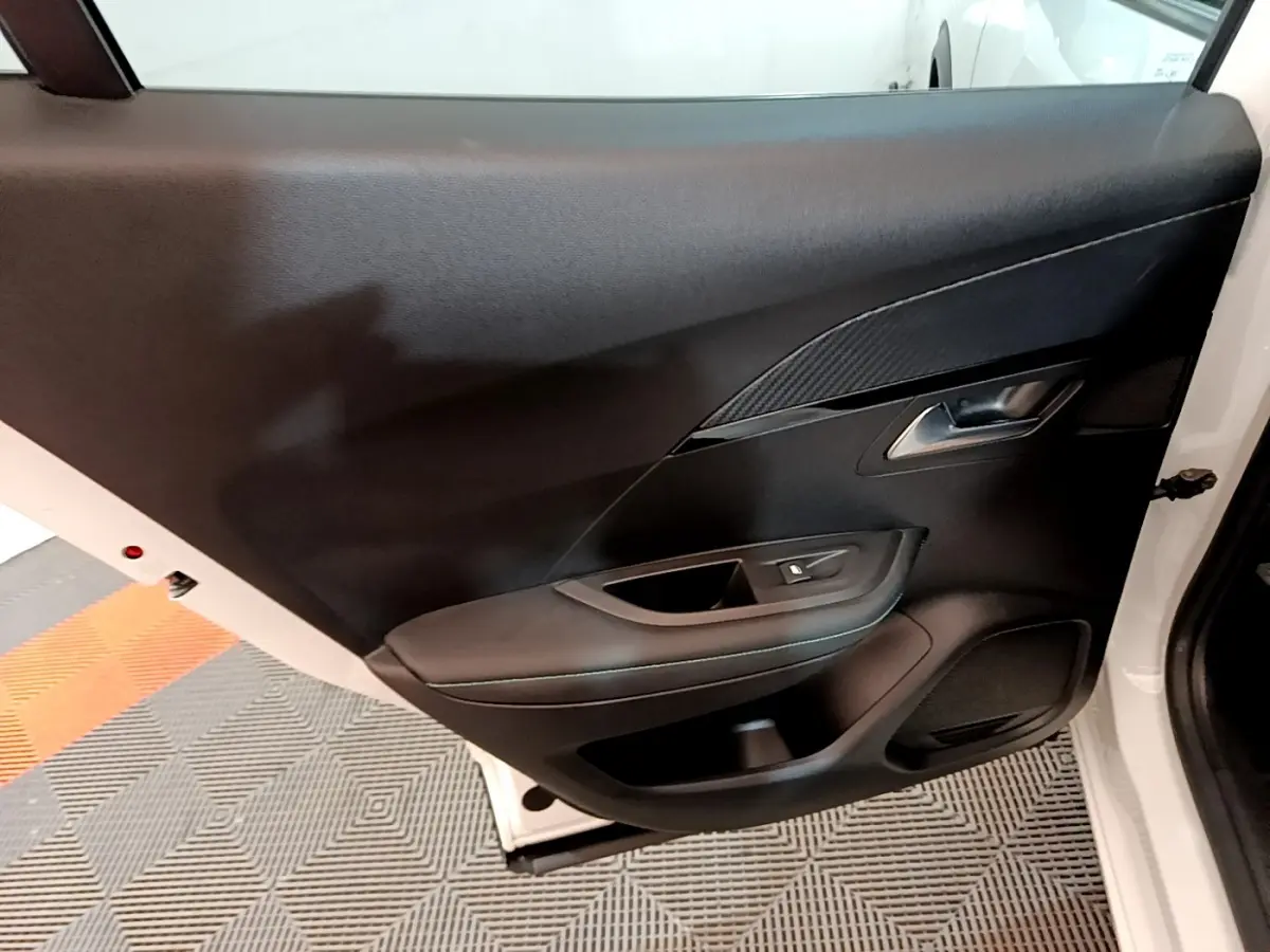 Vue intérieure de la porte arrière droite d'un Peugeot 2008 blanc, avec garniture noire et poignée argentée.