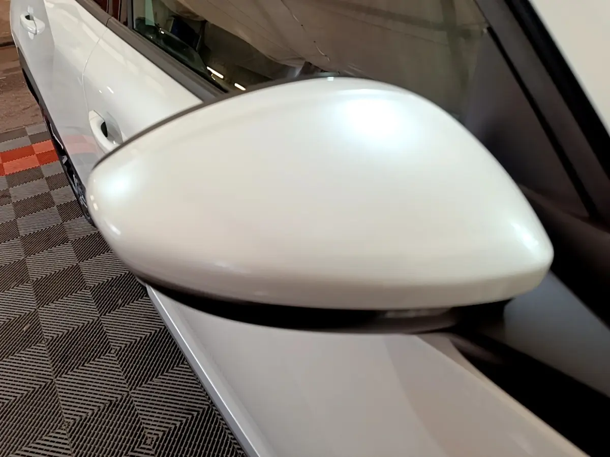Gros plan sur le rétroviseur droit blanc d’un Peugeot 2008 blanc, avec une partie de la portière visible en arrière-plan.