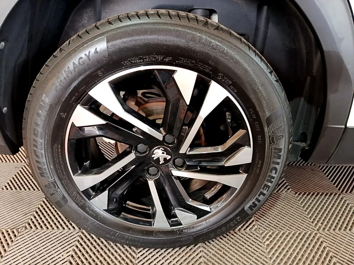 Gros plan sur la roue avant gauche d’un Peugeot 2008 blanc, avec jante alliage noire et argentée au design moderne.