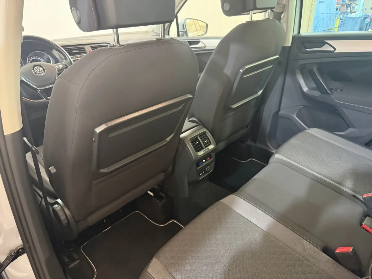 Vue intérieure arrière du Volkswagen Tiguan 2020 montrant les sièges noirs, les dossiers avec tablettes rabattables et la console centrale avec aérateurs.