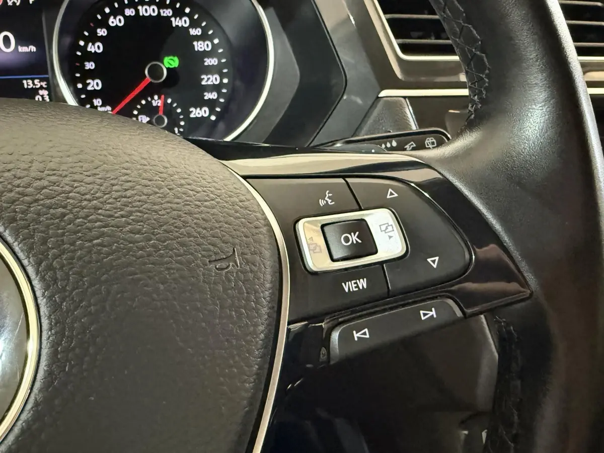 Gros plan sur le volant cuir noir du Volkswagen Tiguan 2020, avec commandes multifonctions et tableau de bord en arrière-plan.