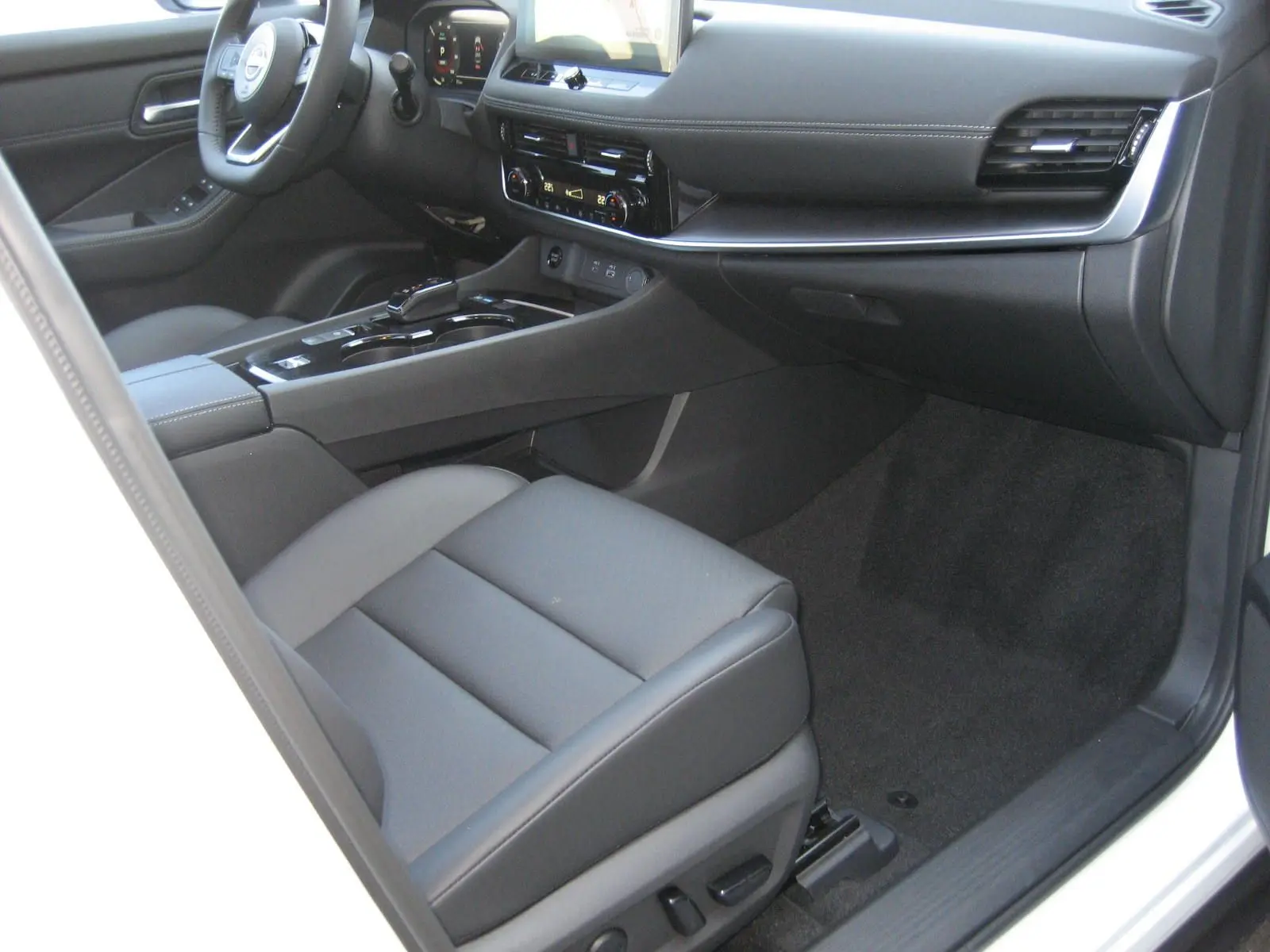 Vue intérieure côté passager du Nissan X-TRAIL blanc nacré, mettant en valeur le tableau de bord moderne et les sièges en cuir gris.