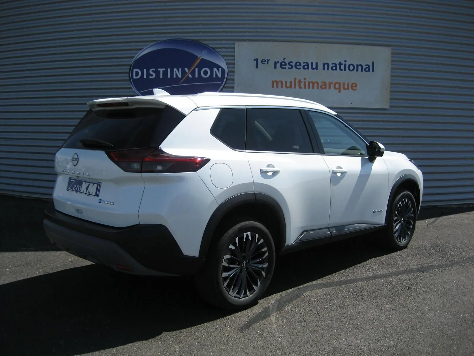 Nissan X-Trail blanc nacré vu en 3/4 arrière droit, avec jantes noires et toit blanc contrasté.