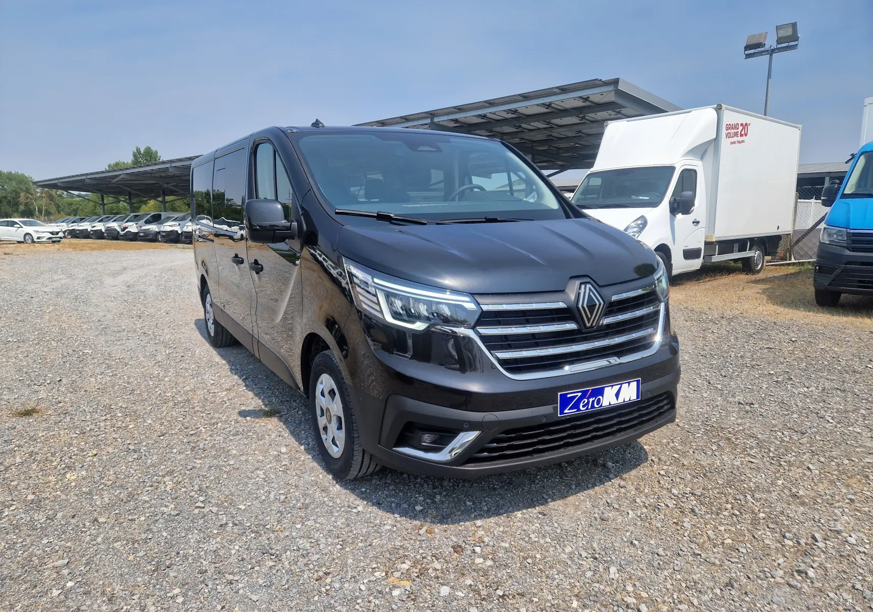Renault Trafic Combi noir vu en 3/4 avant droit sur parking, avec calandre chromée et plaque Zero KM visible.