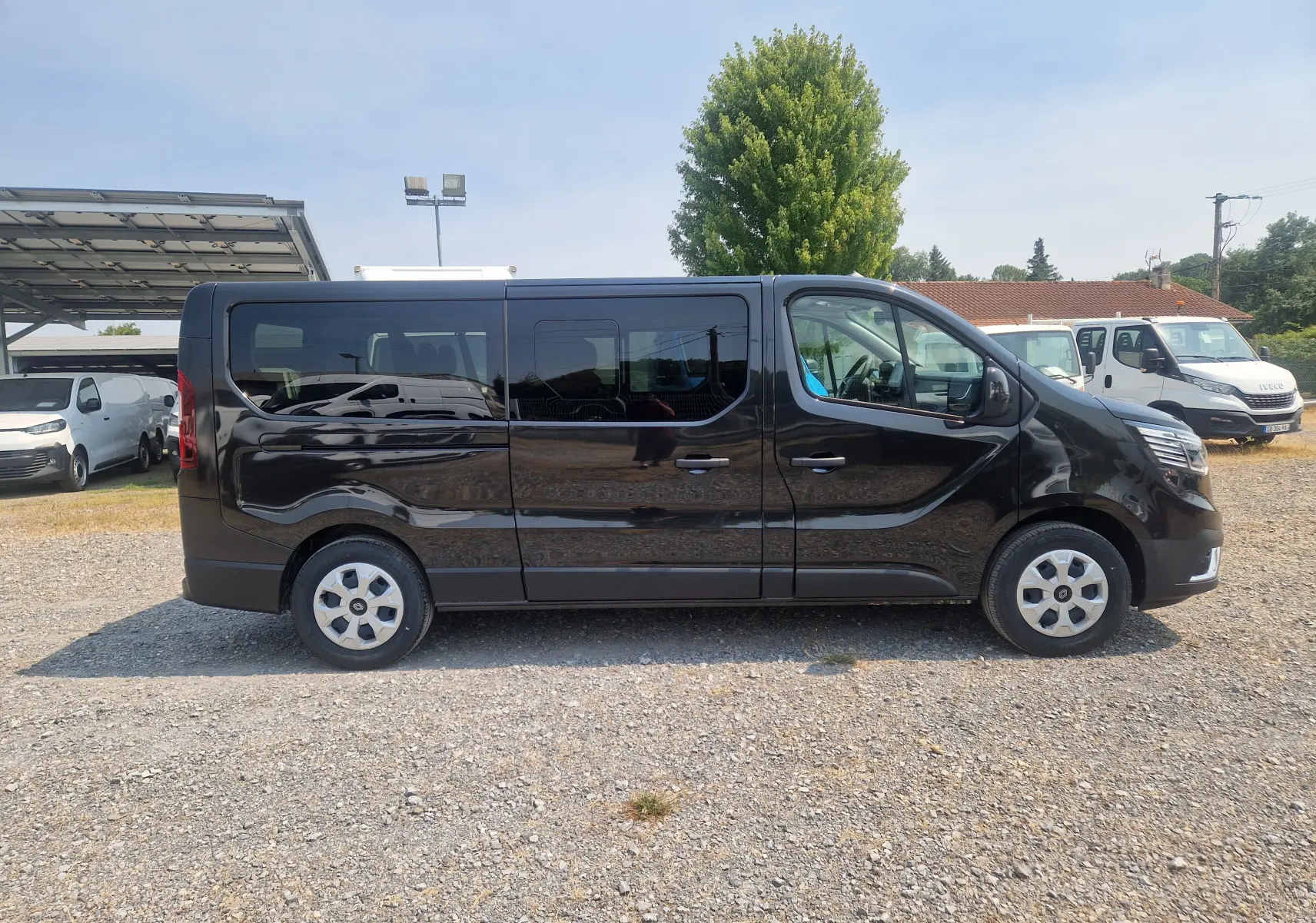 Profil latéral droit d’un Renault Trafic Combi noir 2026, avec vitres teintées et jantes acier, stationné sur un sol gravillonné.