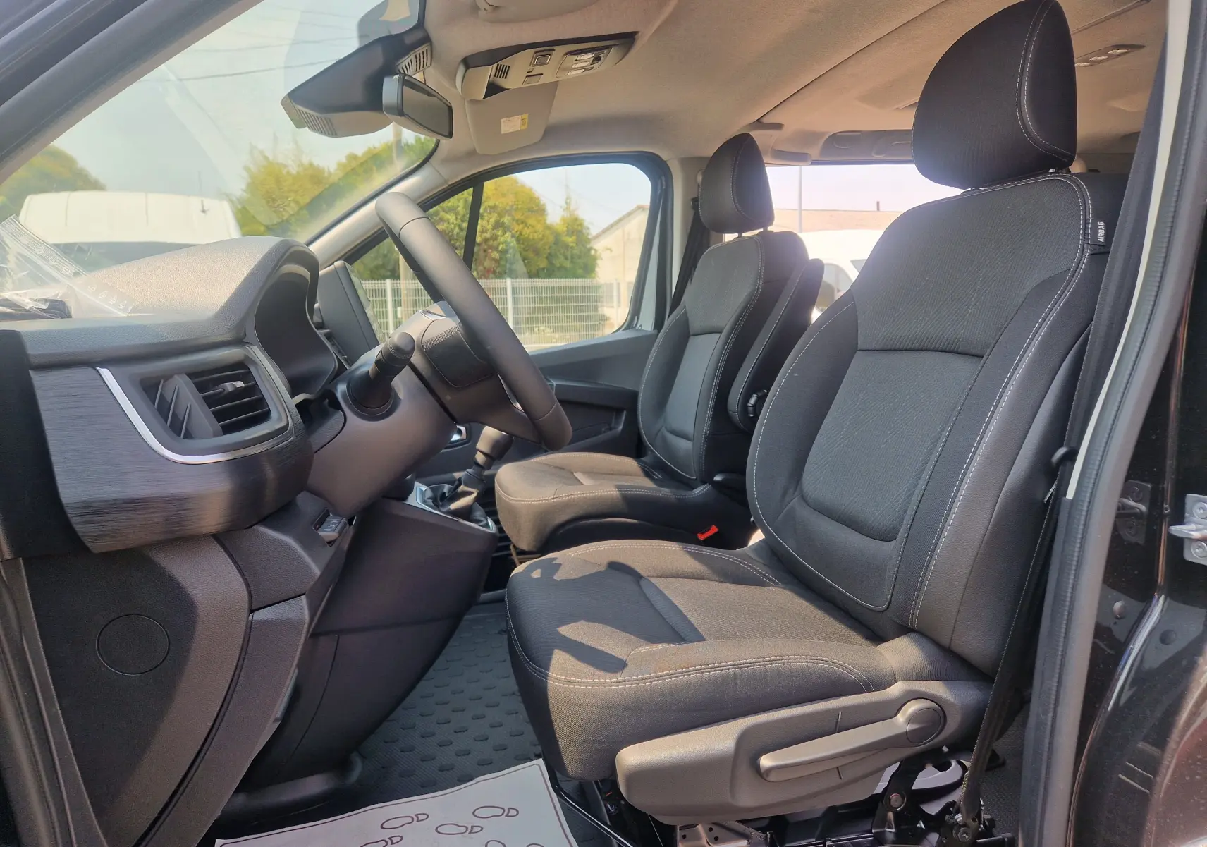 Vue intérieure côté conducteur du Renault Trafic Combi noir 2026, montrant les sièges avant et le tableau de bord.