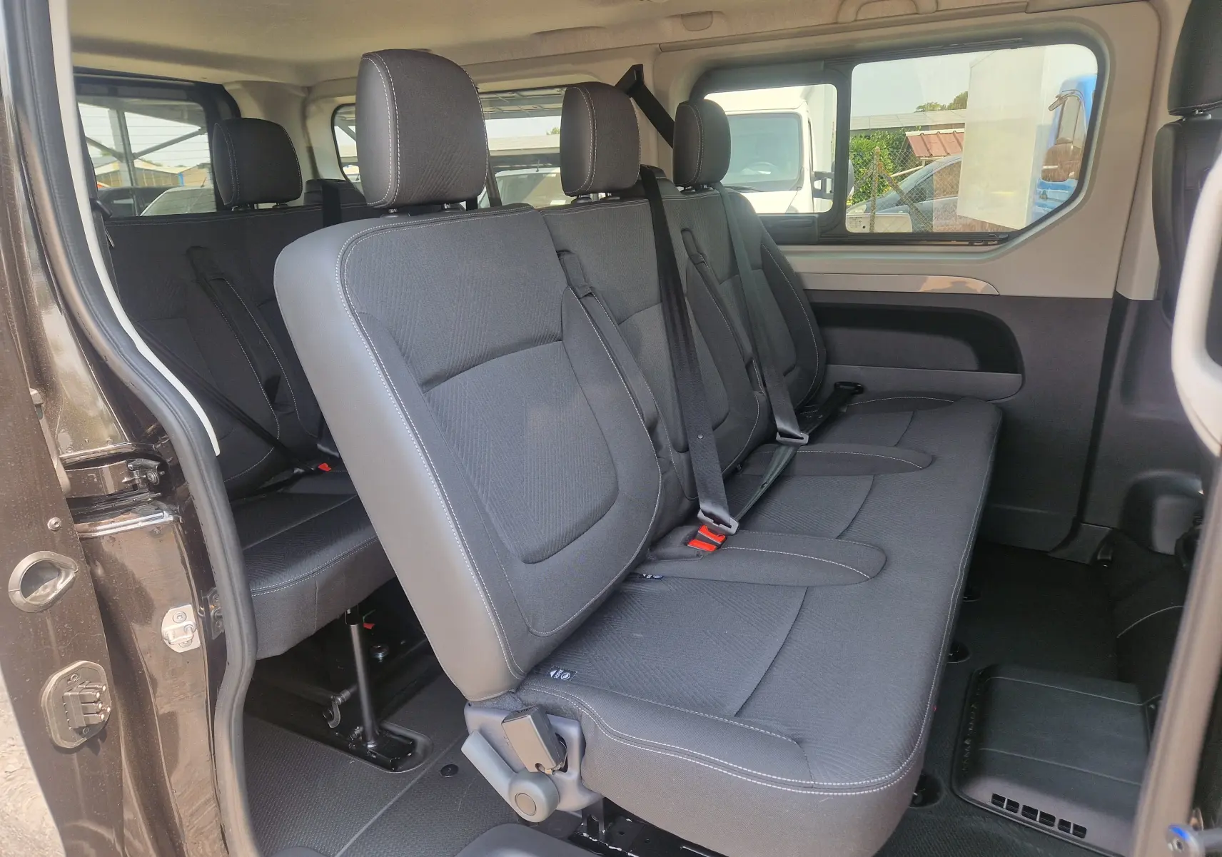 Vue latérale intérieure côté droit du Renault Trafic Combi noir 2026, montrant les sièges passagers en tissu avec ceintures.