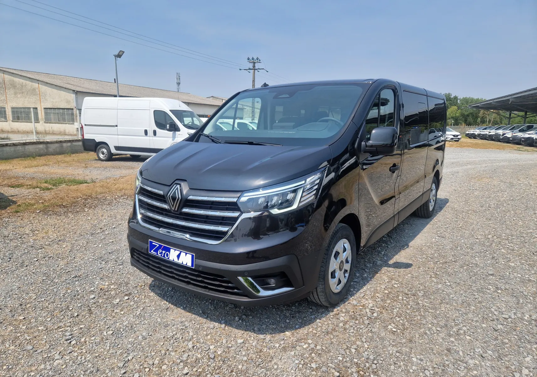 Renault Trafic Combi noir en 3/4 avant droit, avec calandre chromée et phares LED allumés, sur parking extérieur.