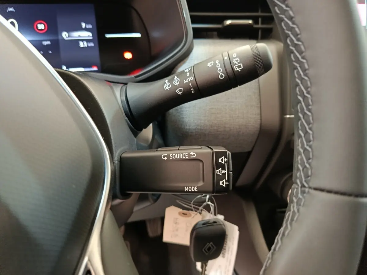 Gros plan sur la commande multifonctions à gauche du volant cuir d’une Renault Clio blanche 2024, tableau de bord en arrière-plan.