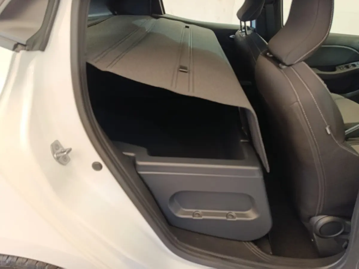 Vue intérieure côté gauche arrière de la Renault Clio blanche 2024 avec banquette rabattue et coffre de rangement visible.