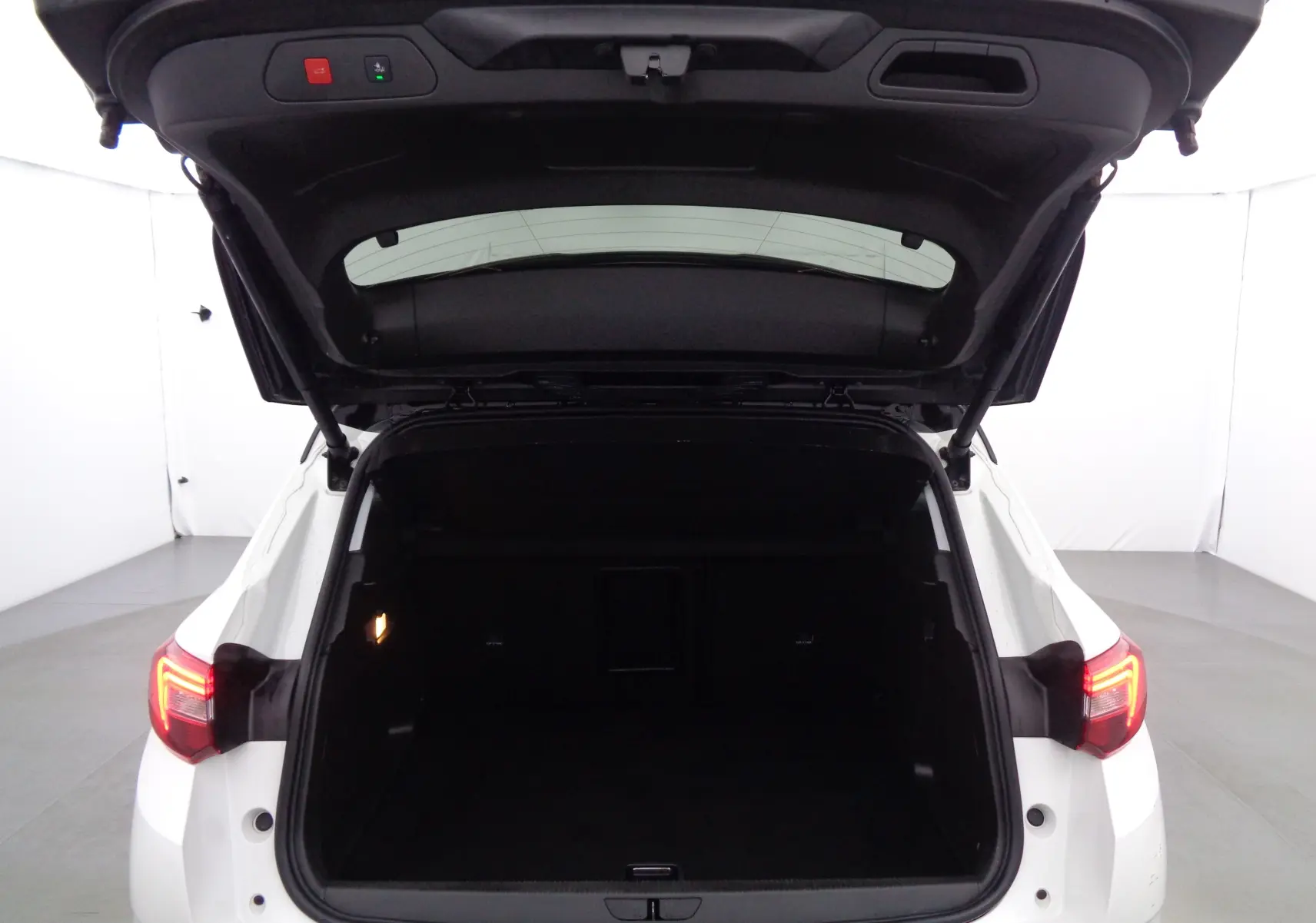 Coffre ouvert vu de l'arrière d'un Opel Grandland X blanc métal avec feux arrière allumés dans un studio.