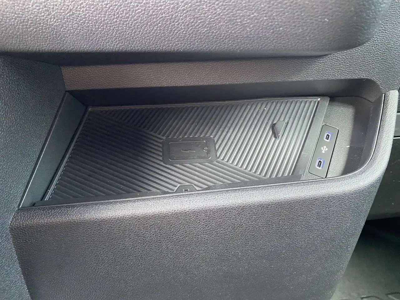 Gros plan sur le chargeur sans fil et les ports USB intégrés dans la console intérieure noire du Renault Master blanc.