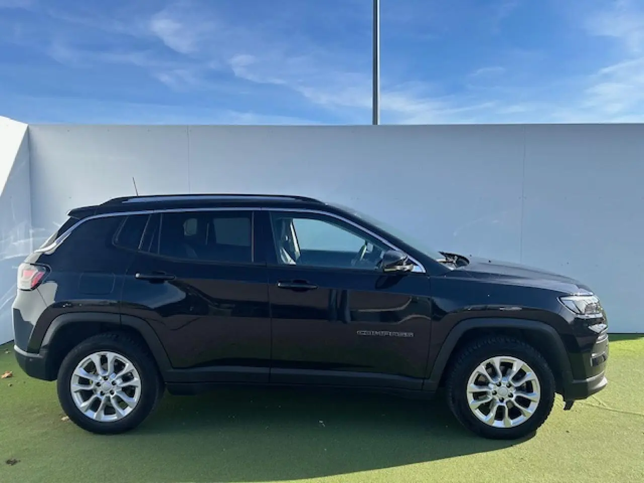 Profil latéral droit d'un Jeep Compass noir métallisé avec jantes alliage et barres de toit longitudinales visibles.