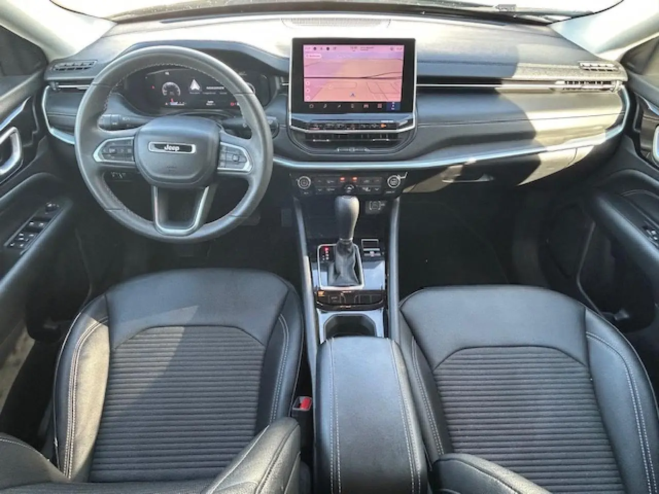 Vue intérieure avant du Jeep Compass noir, mettant en valeur le tableau de bord numérique et la console centrale avec écran tactile.