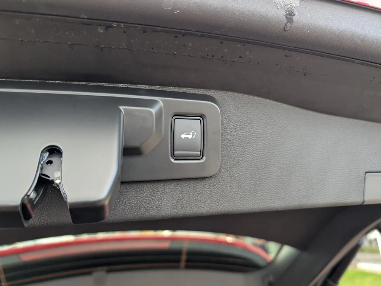 Bouton d'ouverture du hayon électrique sur la face intérieure du coffre d'un Renault Austral rouge métallisé.