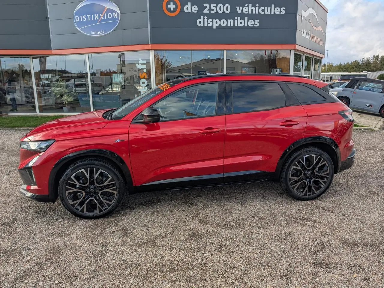 Profil côté gauche d'un Renault Austral rouge métallisé Esprit Alpine avec jantes alliage noires et toit panoramique.