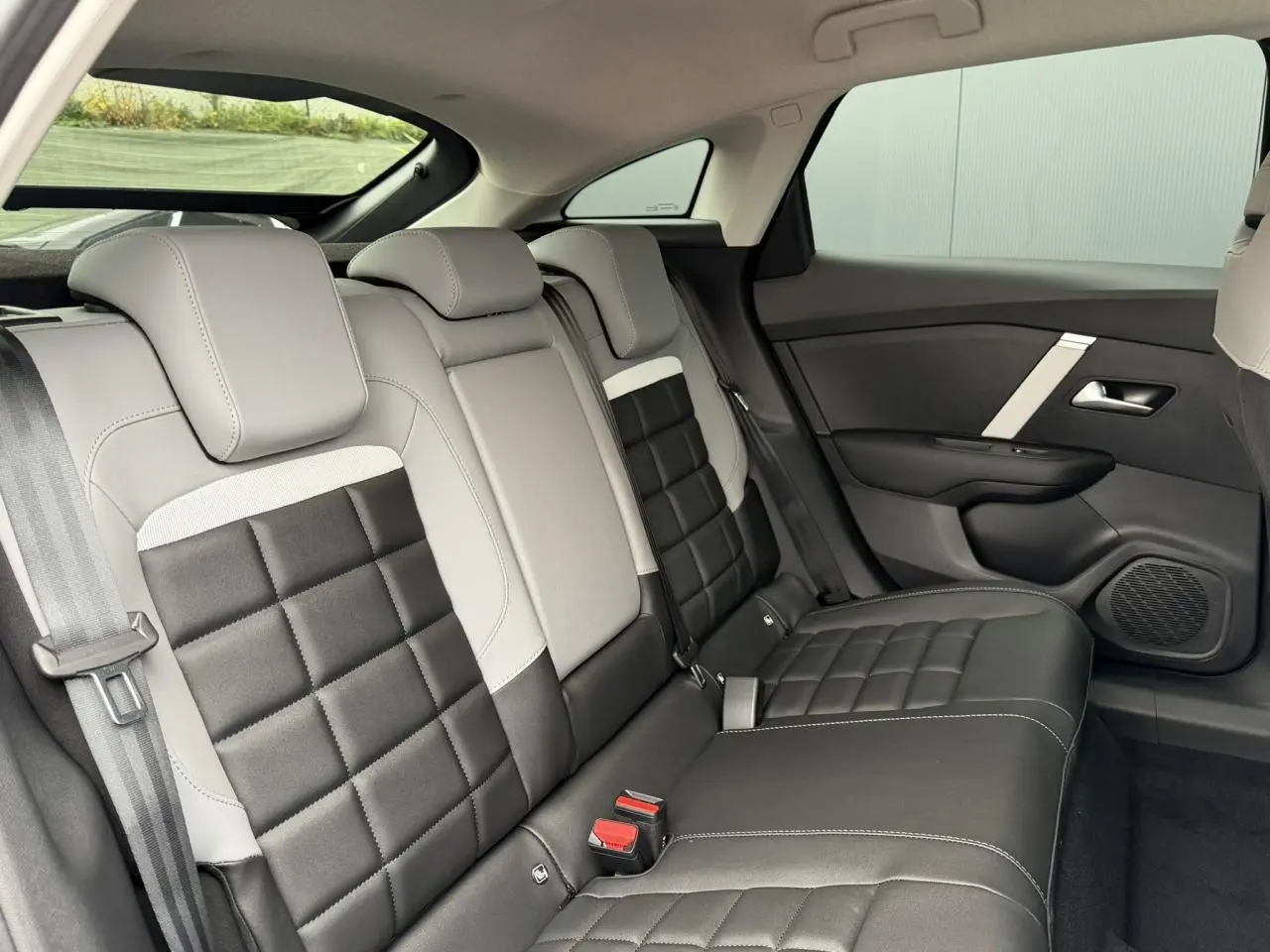 Vue latérale droite des sièges arrière bicolores gris clair et noir de la Citroën C4 NV Hybrid 2025 avec finitions en tissu et cuir.