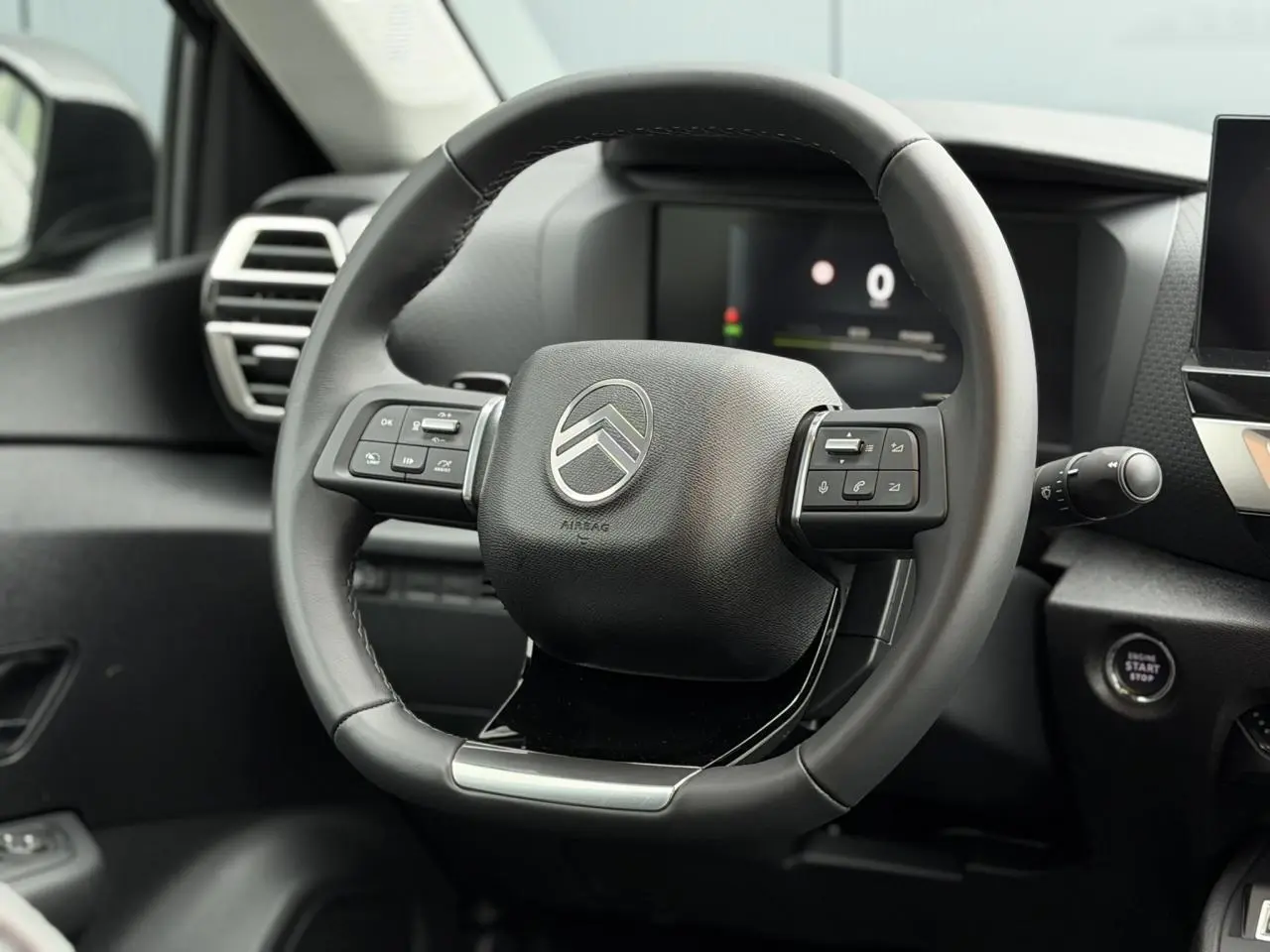 Volant cuir noir de Citroën C4 2025 vu de face, avec commandes intégrées et tableau de bord numérique en arrière-plan.