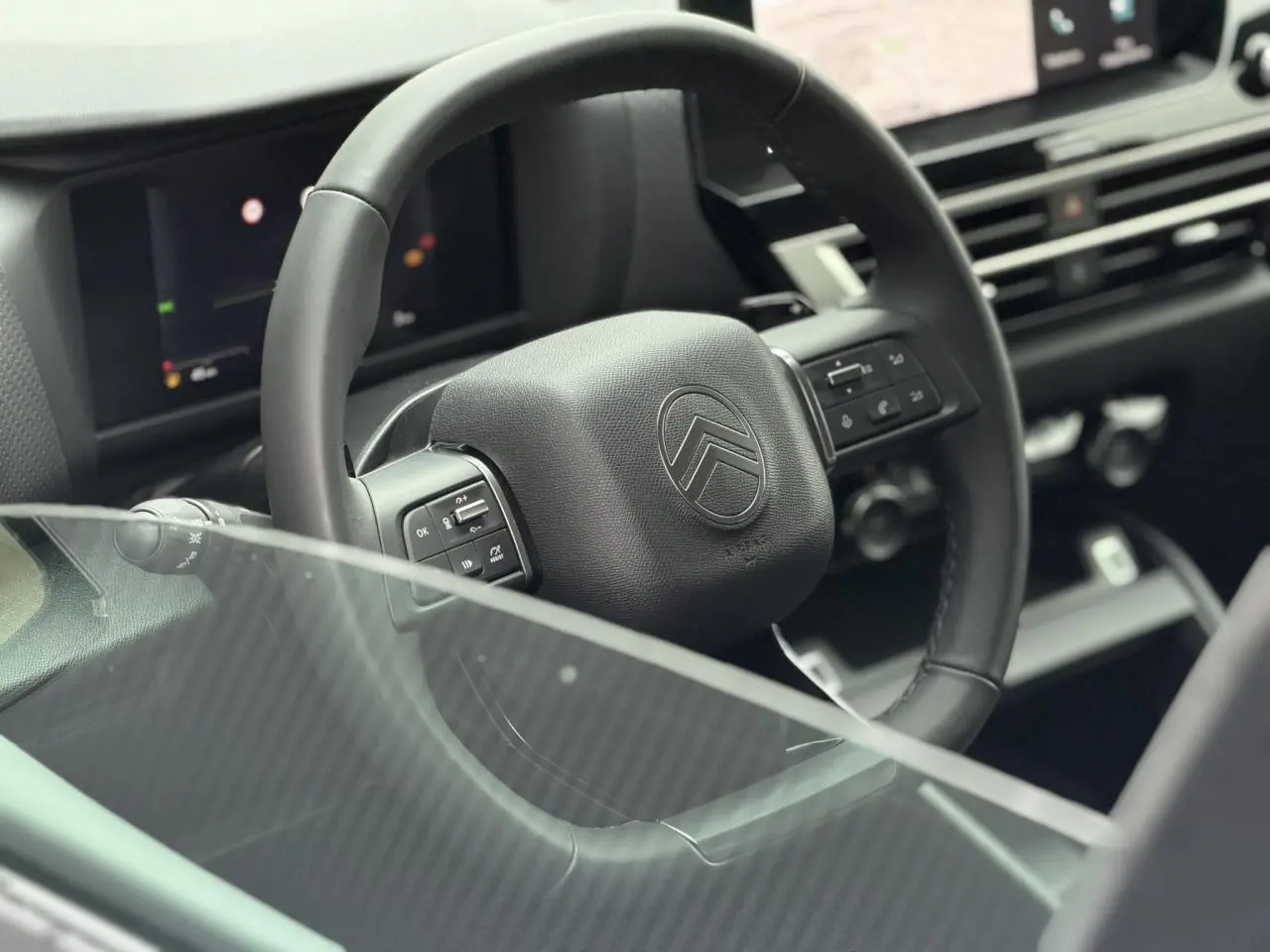 Vue rapprochée du volant cuir noir de la Citroën C4 2025, avec commandes intégrées et tableau de bord numérique en arrière-plan.