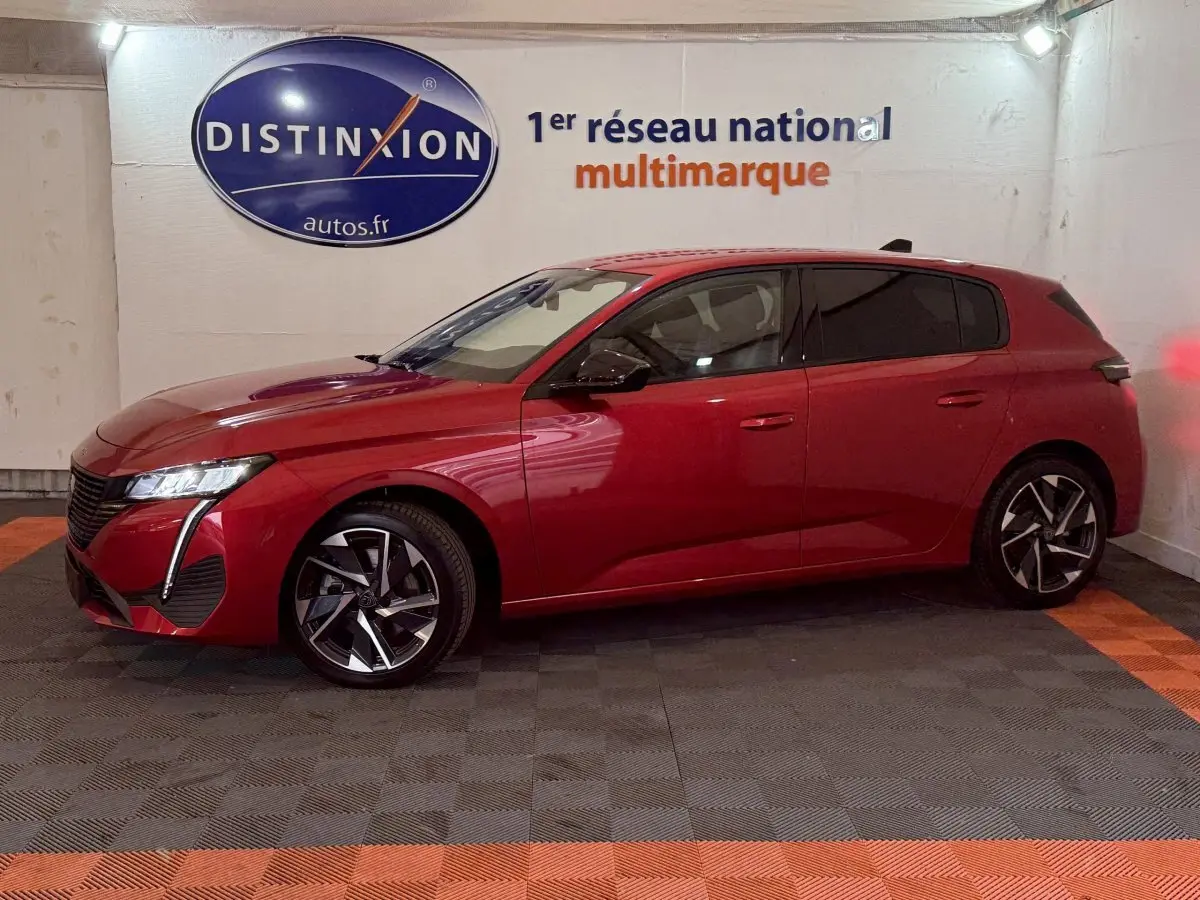 Peugeot 308 BlueHDi 130 AUTO8 Allure rouge vue de profil côté gauche dans un garage avec logo Distinxion en arrière-plan.