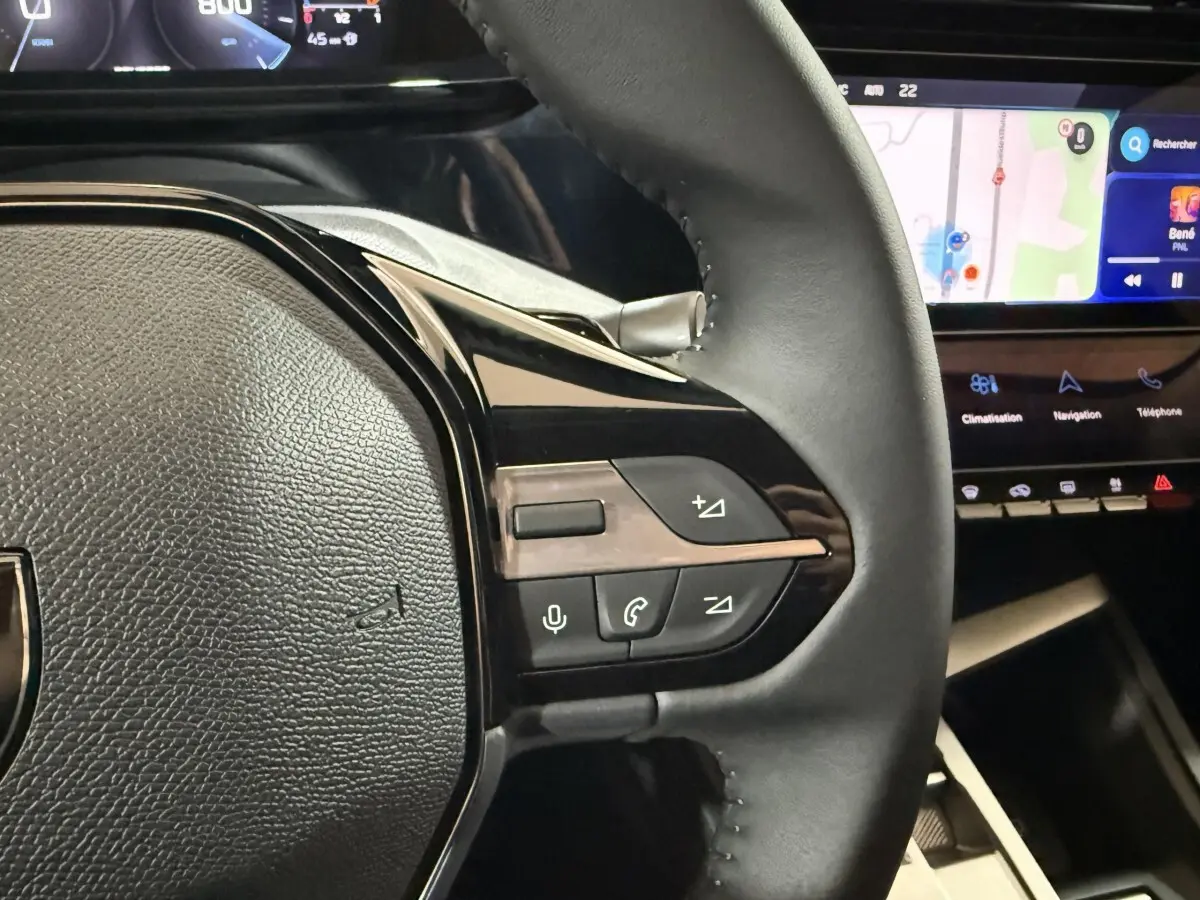 Gros plan sur le volant cuir multifonctions de la Peugeot 308 rouge, avec écran tactile et commandes intégrées visibles.