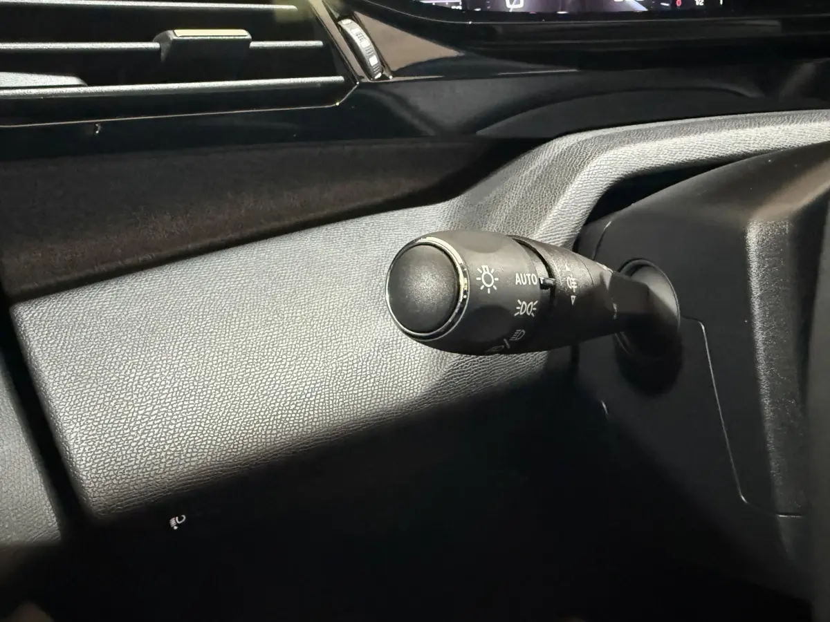 Gros plan sur la commande des phares à gauche du volant dans l’habitacle noir de la Peugeot 308 rouge 2025.