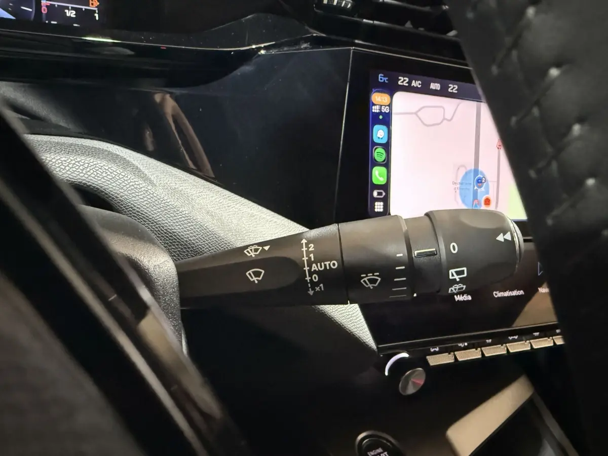 Gros plan sur la commande d’essuie-glace côté gauche du tableau de bord noir d’une Peugeot 308 rouge 2025.