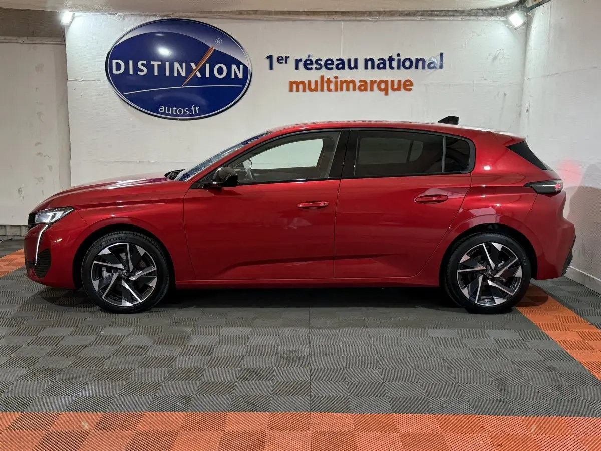 Profil latéral droit d'une Peugeot 308 rouge 2025, avec jantes alliage et vitres teintées, en intérieur showroom.