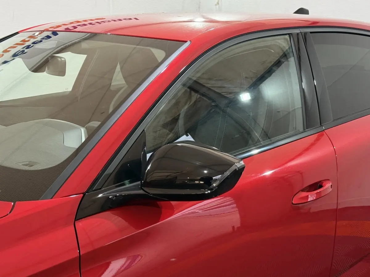 Vue rapprochée du côté gauche avant de la Peugeot 308 rouge, avec rétroviseur noir brillant et poignée de porte intégrée.