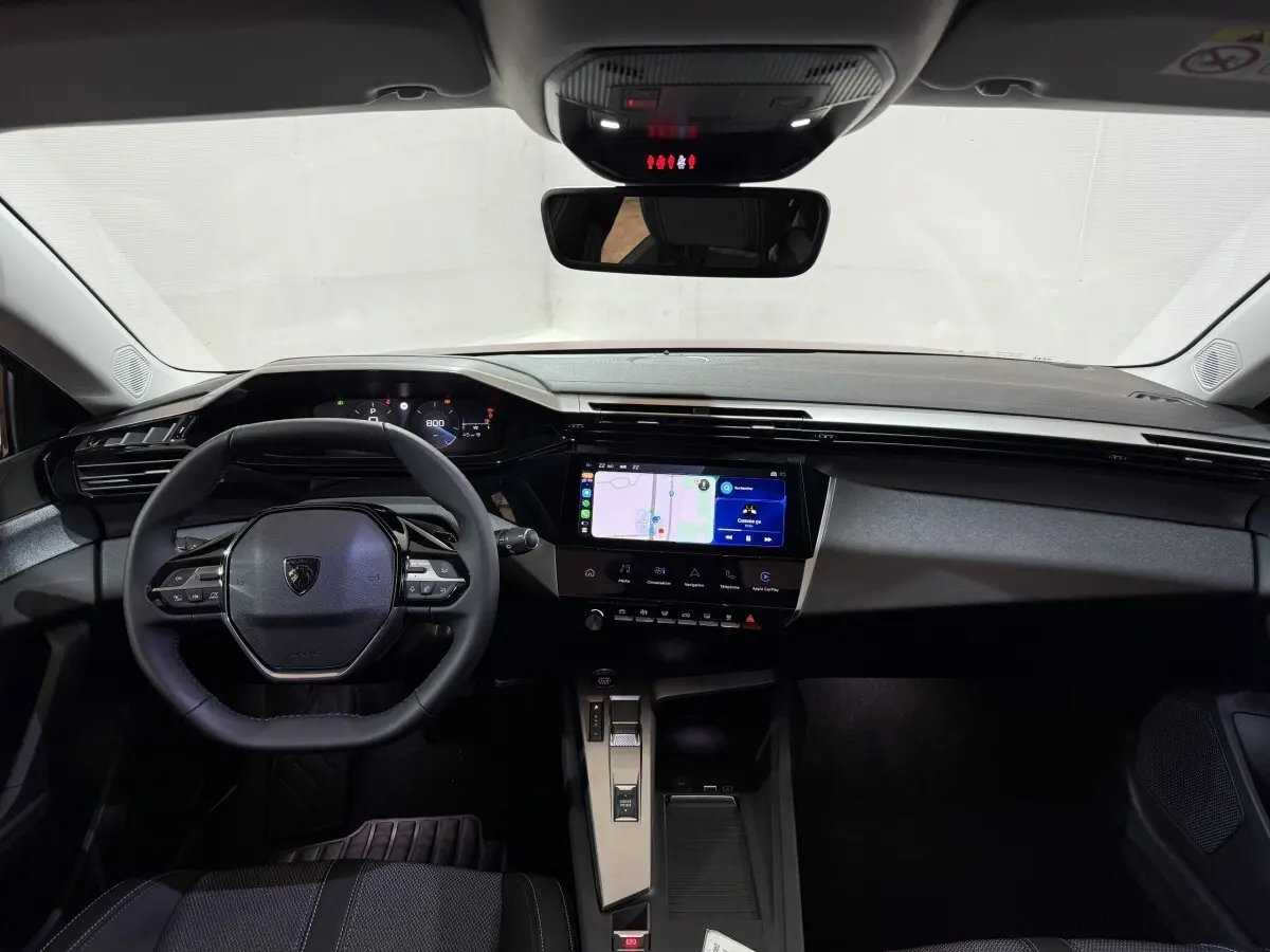 Vue intérieure frontale du tableau de bord et volant cuir multifonctions de la Peugeot 308 2025, écran tactile central allumé.