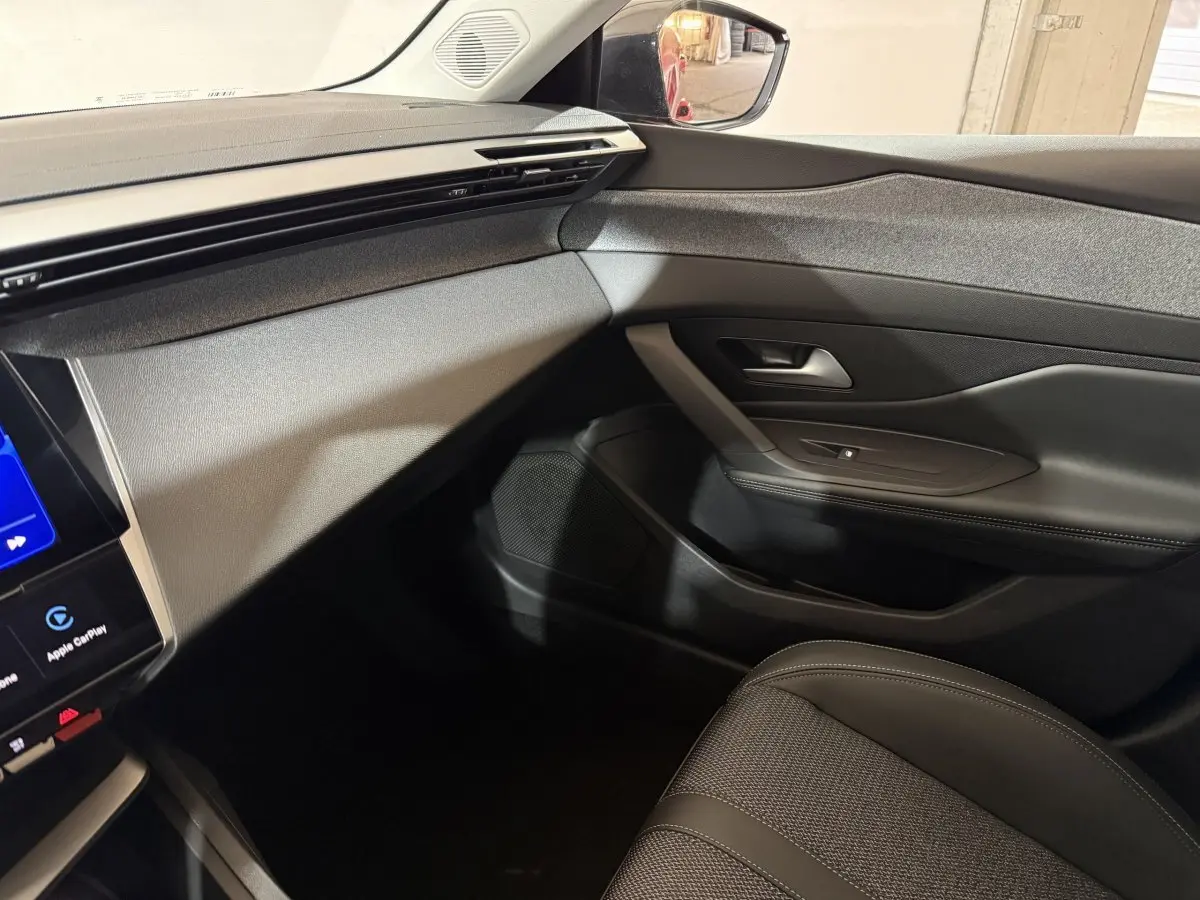 Vue intérieure côté passager du tableau de bord et porte noire de la Peugeot 308 rouge, finition Allure 2025.