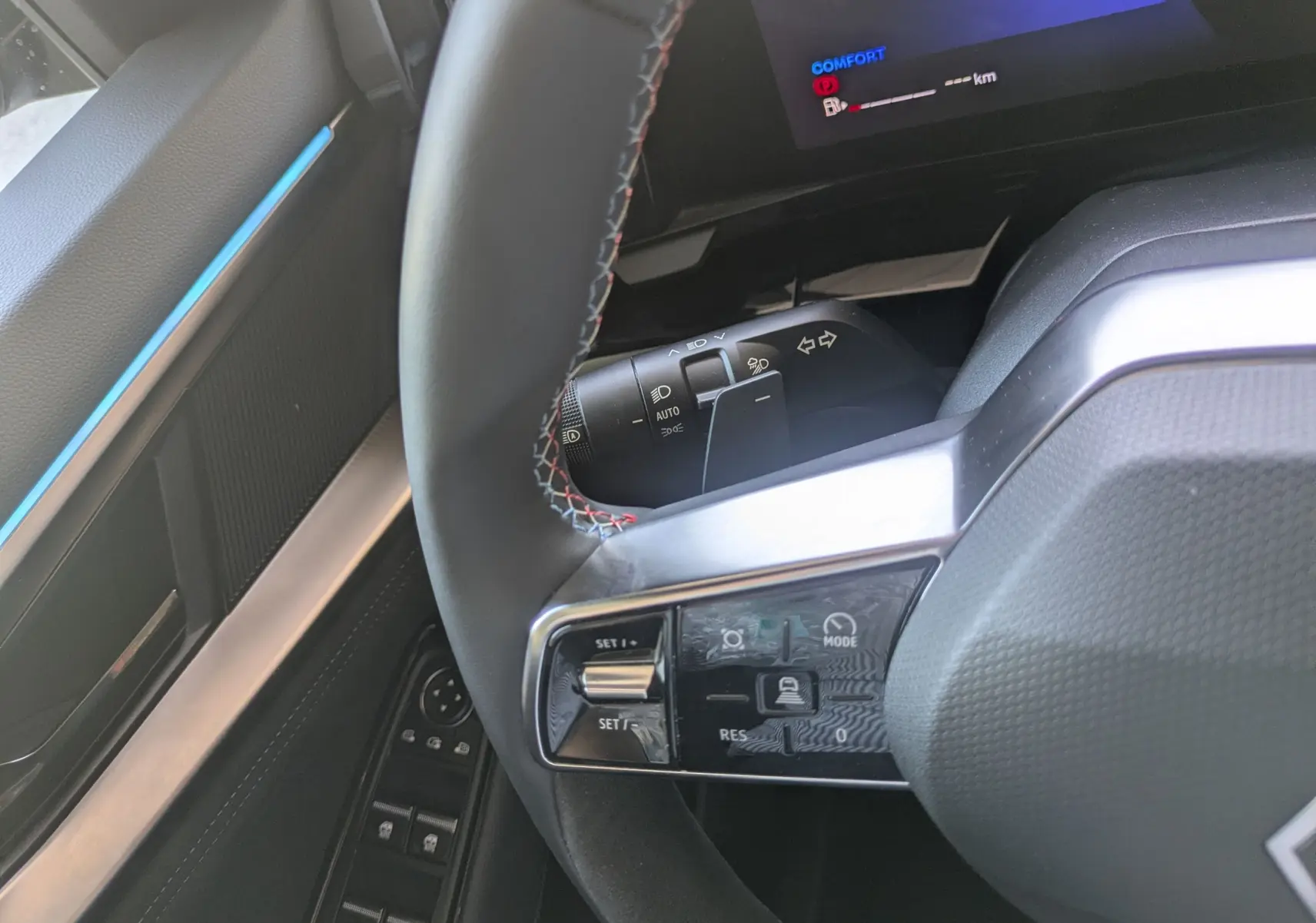 Gros plan sur le volant et la commande multifonction du Renault Espace VI E-Tech noir, avec surpiqûres bleues visibles.