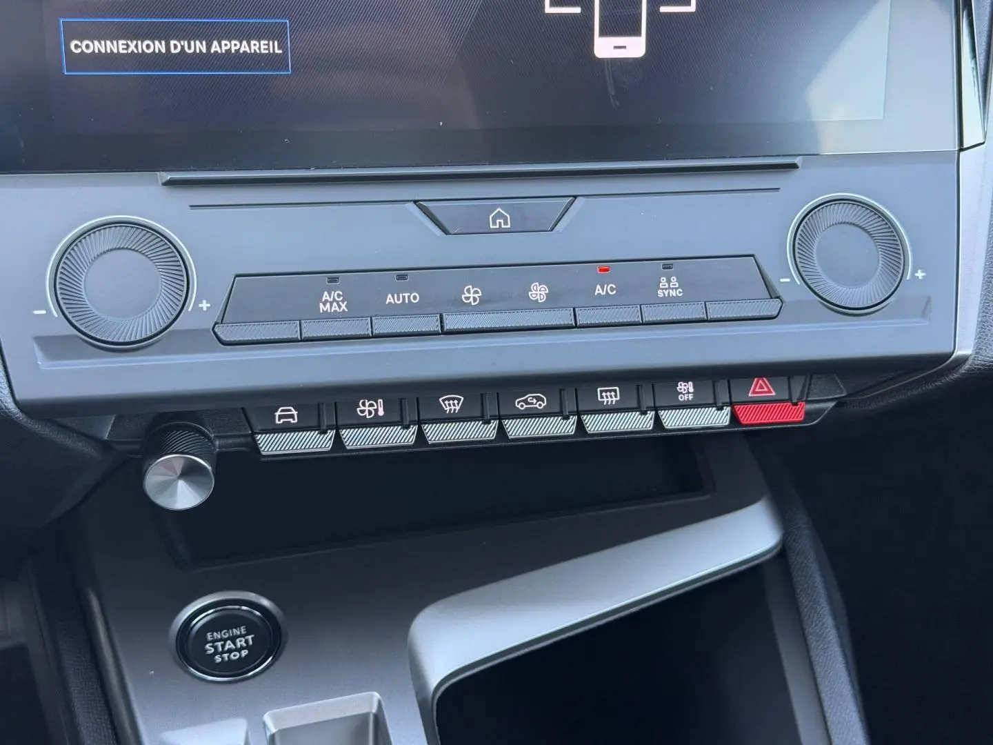 Vue rapprochée de la console centrale de la Peugeot e-308 noire, avec commandes climatisation et bouton start/stop visibles.