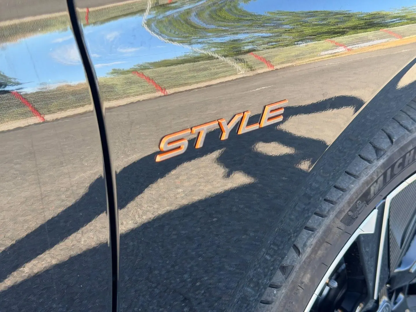 Détail de l’inscription Style orange sur la carrosserie noire Perla Nera d’une Peugeot e-308, près de la roue avant droite.