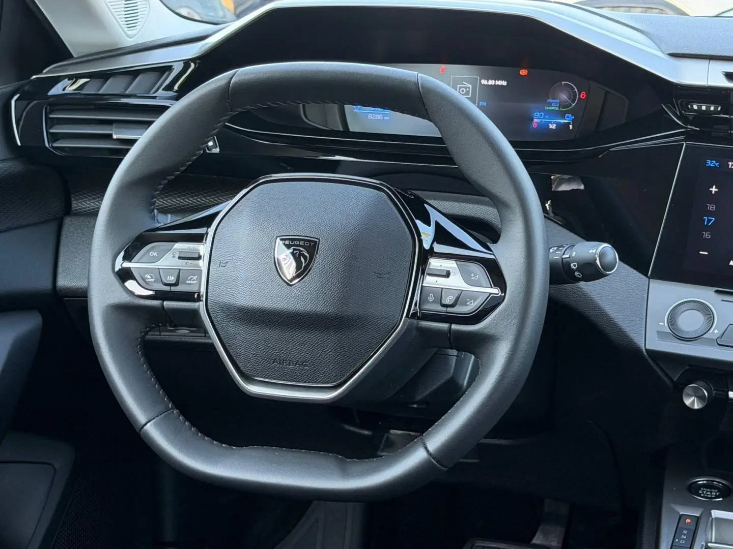 Vue rapprochée du volant multifonction noir de la Peugeot e-308 2025 avec tableau de bord numérique en arrière-plan.