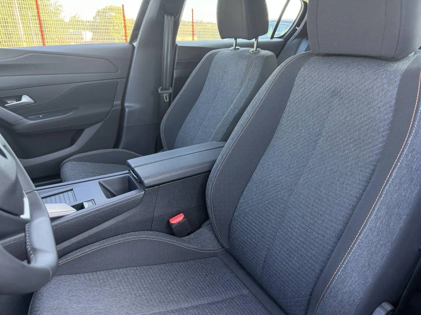 Vue intérieure rapprochée des sièges avant en tissu gris avec surpiqûres orange dans une Peugeot 308 e-308 2025.