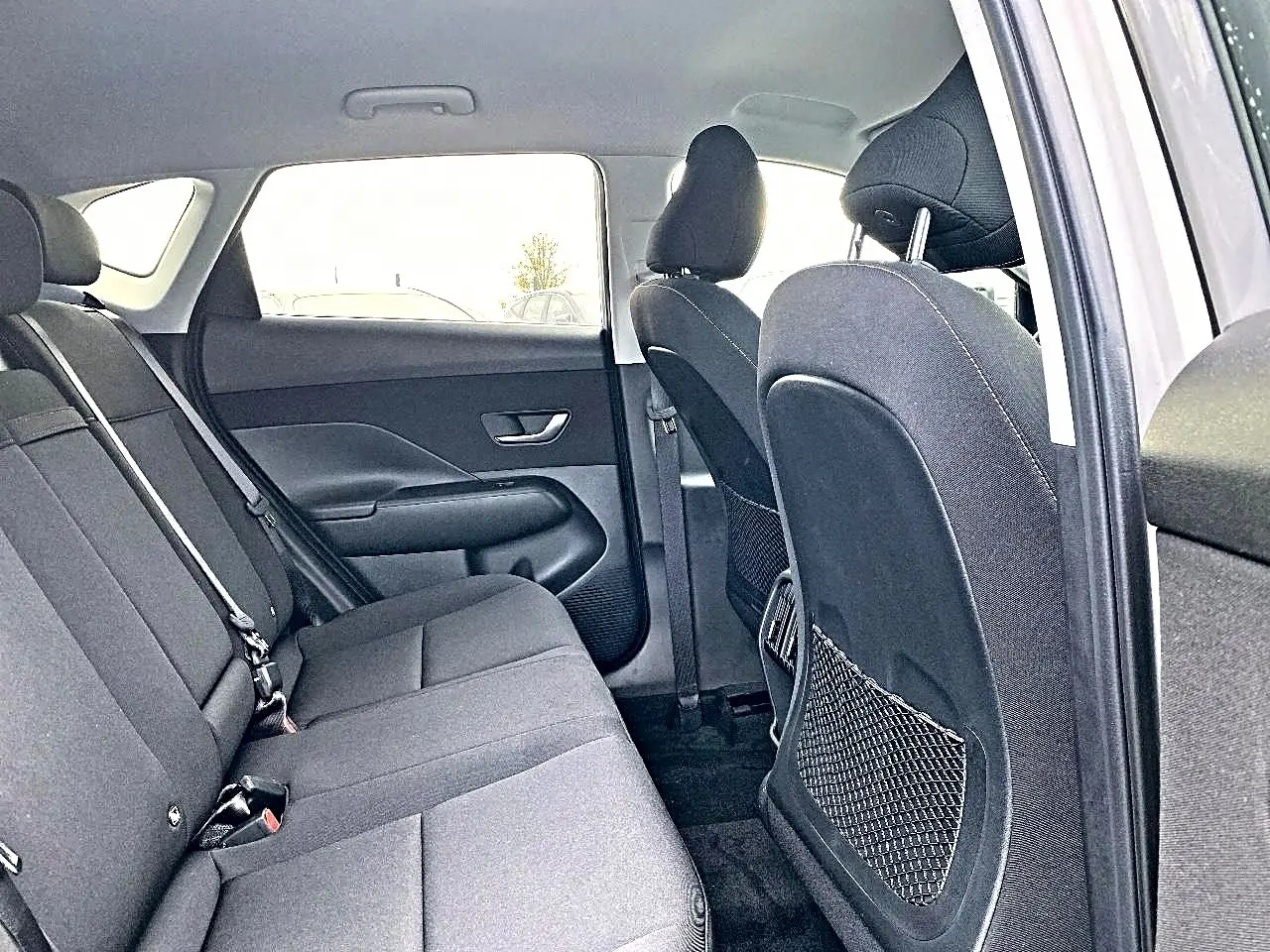 Vue intérieure côté droit sur la banquette arrière grise du Hyundai Kona 2025 avec appuie-têtes et porte arrière ouvert.