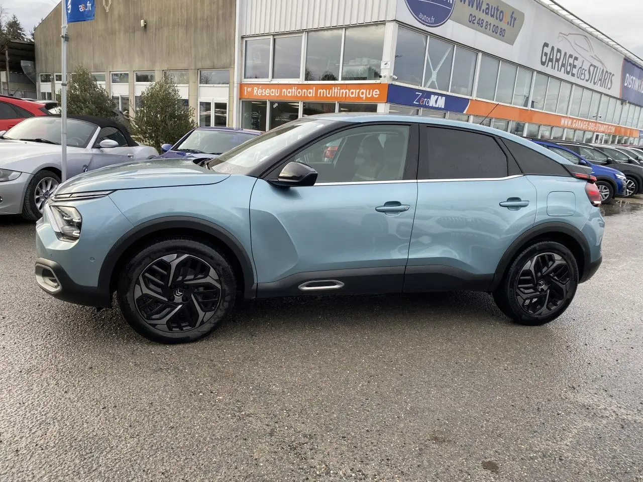 Profil côté gauche d'une Citroën C4 2021 bleu Iceland avec toit noir et jantes noires au garage.